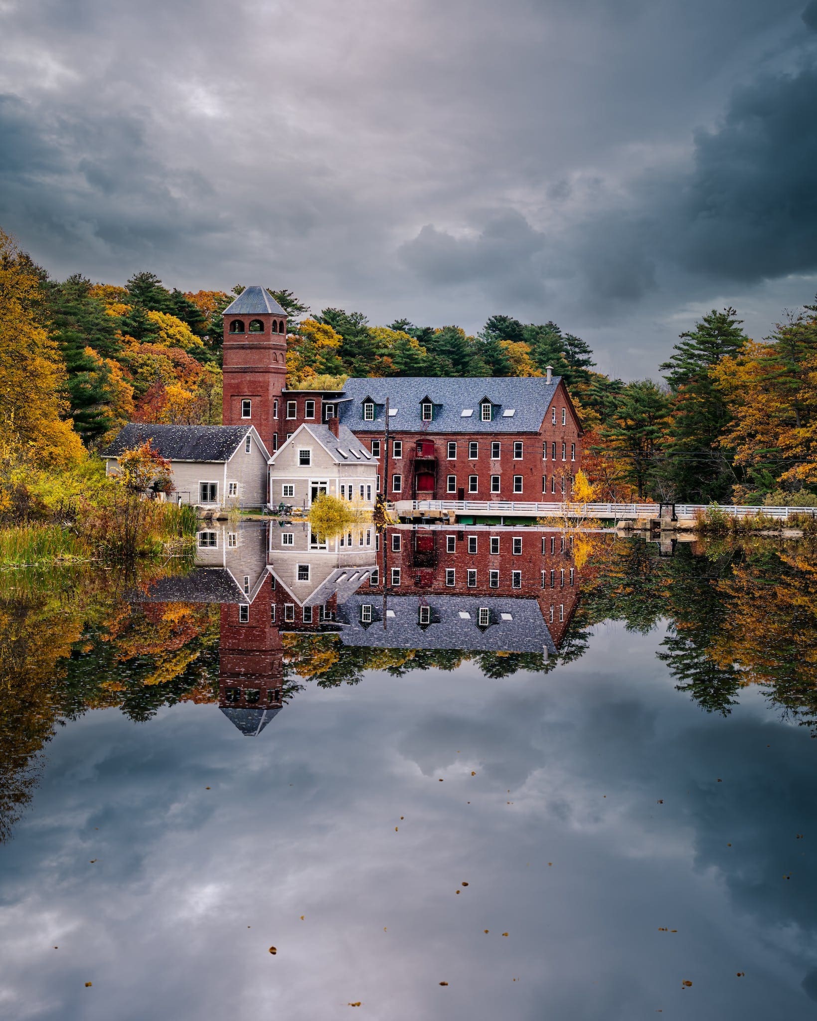 Peaceful lake reflecting aged houses and lush autumn trees under overcast sky