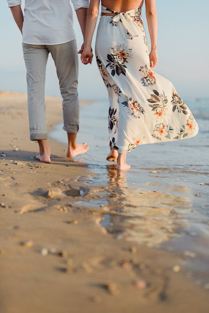 Anonymous romantic couple holding hand and walking on sandy seashore